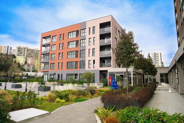 A modern multi-story building with balconies, a landscaped courtyard with seating, and a clear sky. - The Superior Living Kağıthane (Istanbul)