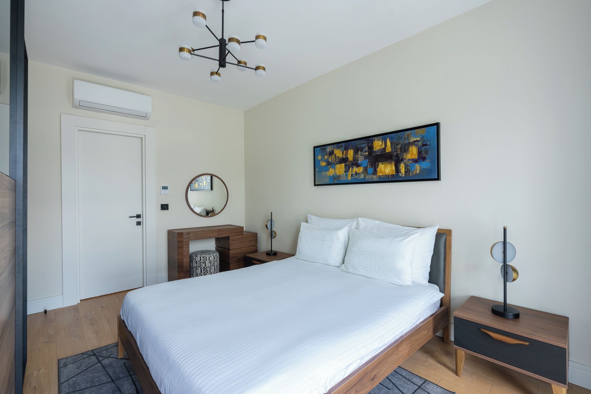 A bedroom with a bed, bedside tables, a mirror, a painting, and a ceiling light fixture.