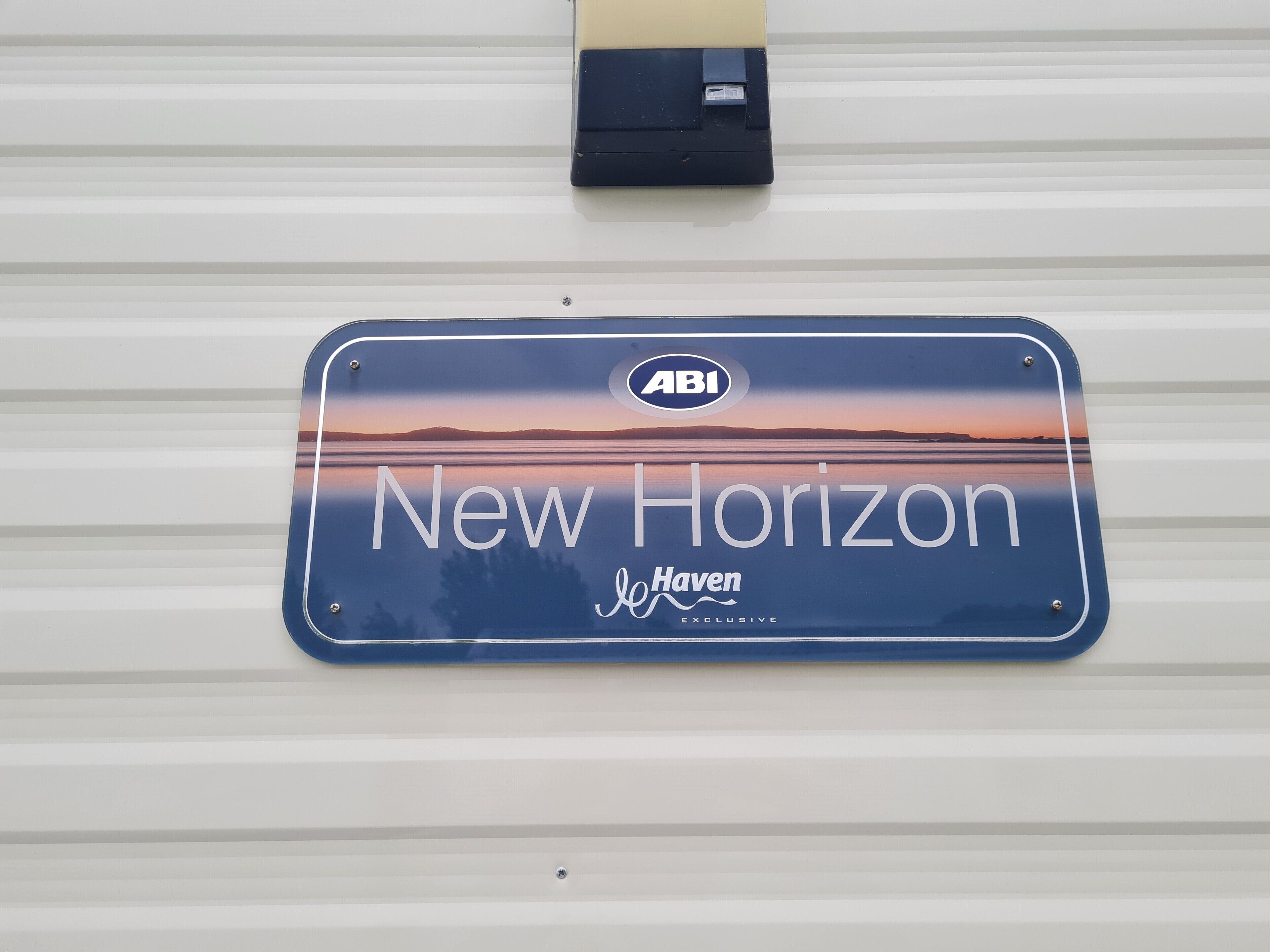Un panneau bleu portant les inscriptions « New Horizon » et « Haven Exclusive », fixé sur un mur en métal ondulé blanc.