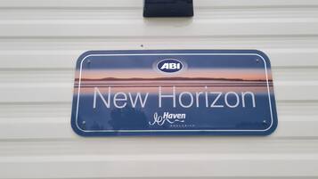 Un panneau bleu portant les inscriptions « New Horizon » et « Haven Exclusive », fixé sur un mur en métal ondulé blanc.