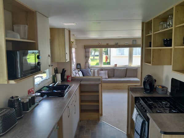 A compact kitchen with a stove, microwave, and sink. There is a seating area with a sofa and a window overlooking the yard. - Ye Old'e Man - Sleeps 6 & Pet Friendly (Grange-over-Sands)