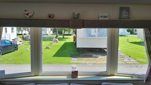 Een kamer met een groot raam dat uitkijkt op een gazon en een stacaravan.