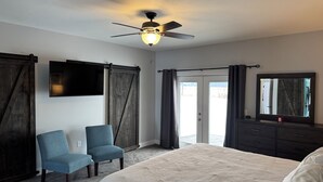 A bedroom with a bed, a chair, a dresser, a ceiling fan, a TV, and a sliding door.