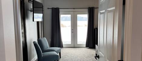 A room with a grey carpet, a blue chair, a ceiling fan, and a door with a view to the outside.