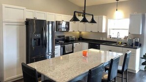 A modern kitchen with white cabinets, stainless steel appliances, a granite countertop, and black bar stools.