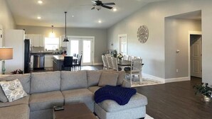 A spacious living room with a large sectional sofa, a dining area with a round table, and a kitchen in the background.
