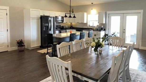 A modern kitchen with white cabinets, a black refrigerator, and a dining area with a wooden table and white chairs.