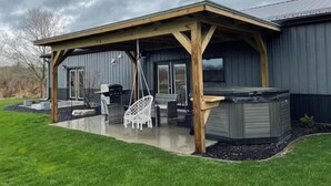 A covered patio area with outdoor furniture, a hot tub, and a large window.