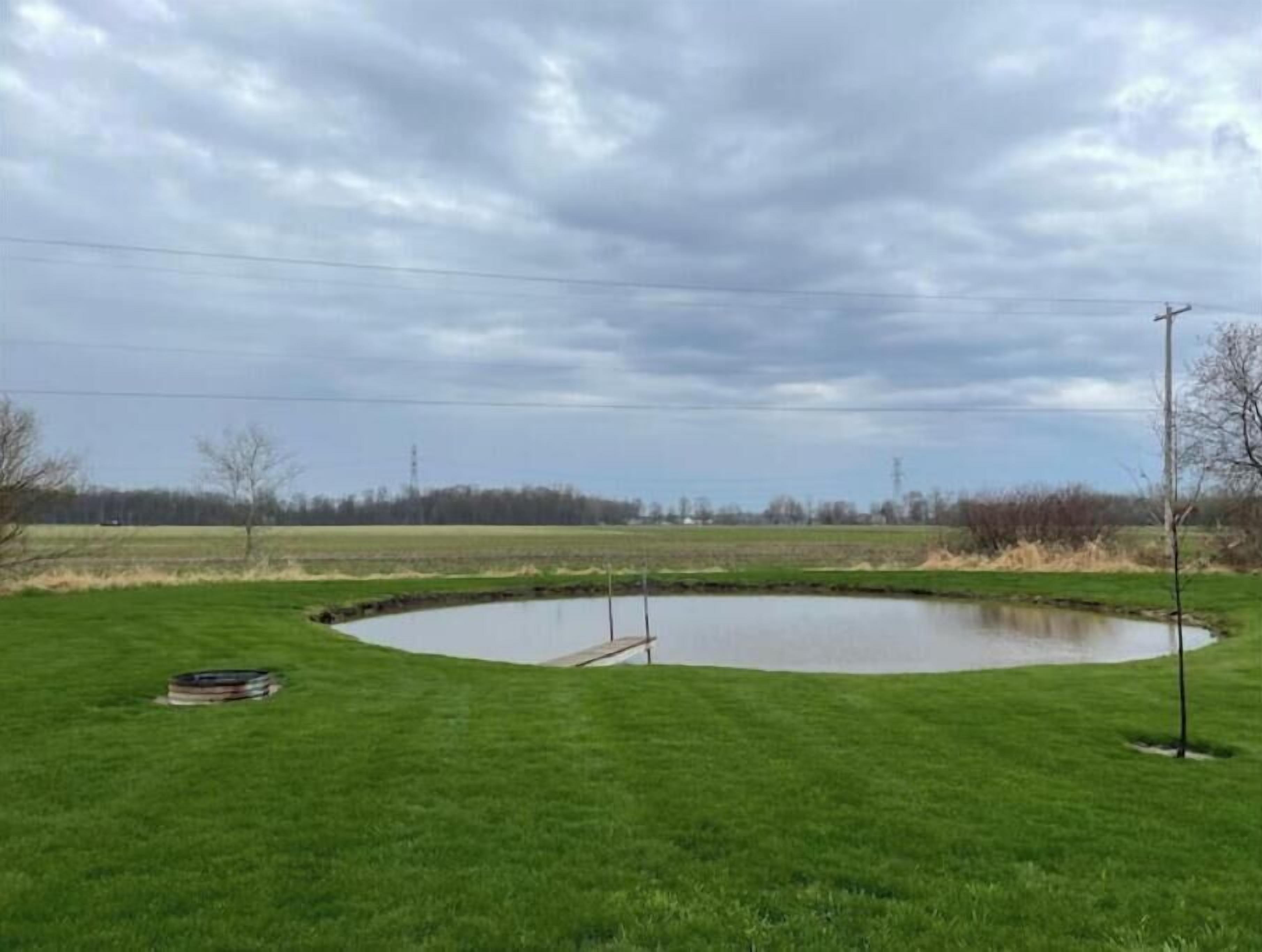 Ein kreisförmiger Teich in einer grünen Wiese mit einer Bank und einer Stromleitung in der Nähe.