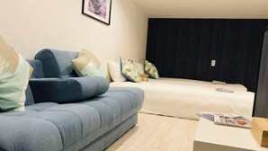 Ett modernt sovrum med en blå soffa, en vit säng och ett litet bord med en tidning på.