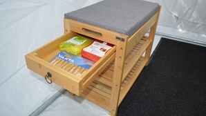 A wooden storage unit with a grey cushion top, containing various items including a yellow package, a red package, and a blue box. - Bubble Tent Loiret: nature and comfort, close to the Loire castles (Chuelles)