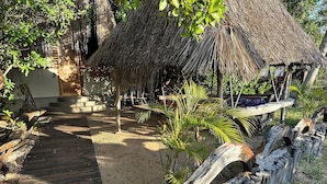 A wooden pathway leading to a thatched-roof structure surrounded by greenery.