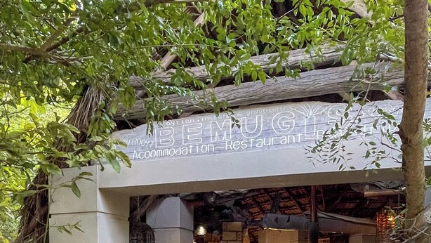 A rustic restaurant entrance with a stone archway, wooden beams, and a signboard.