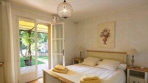 Une chambre à coucher avec un lit, des tables de chevet, un lustre, une fenêtre avec des rideaux et un tableau au mur.