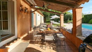 Une terrasse extérieure dotée d’une pergola en bois, d’une piscine et d’un espace repas avec des chaises et des tables.