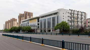 A multi-story building with a modern facade, a wide road in front, and a blue barrier.