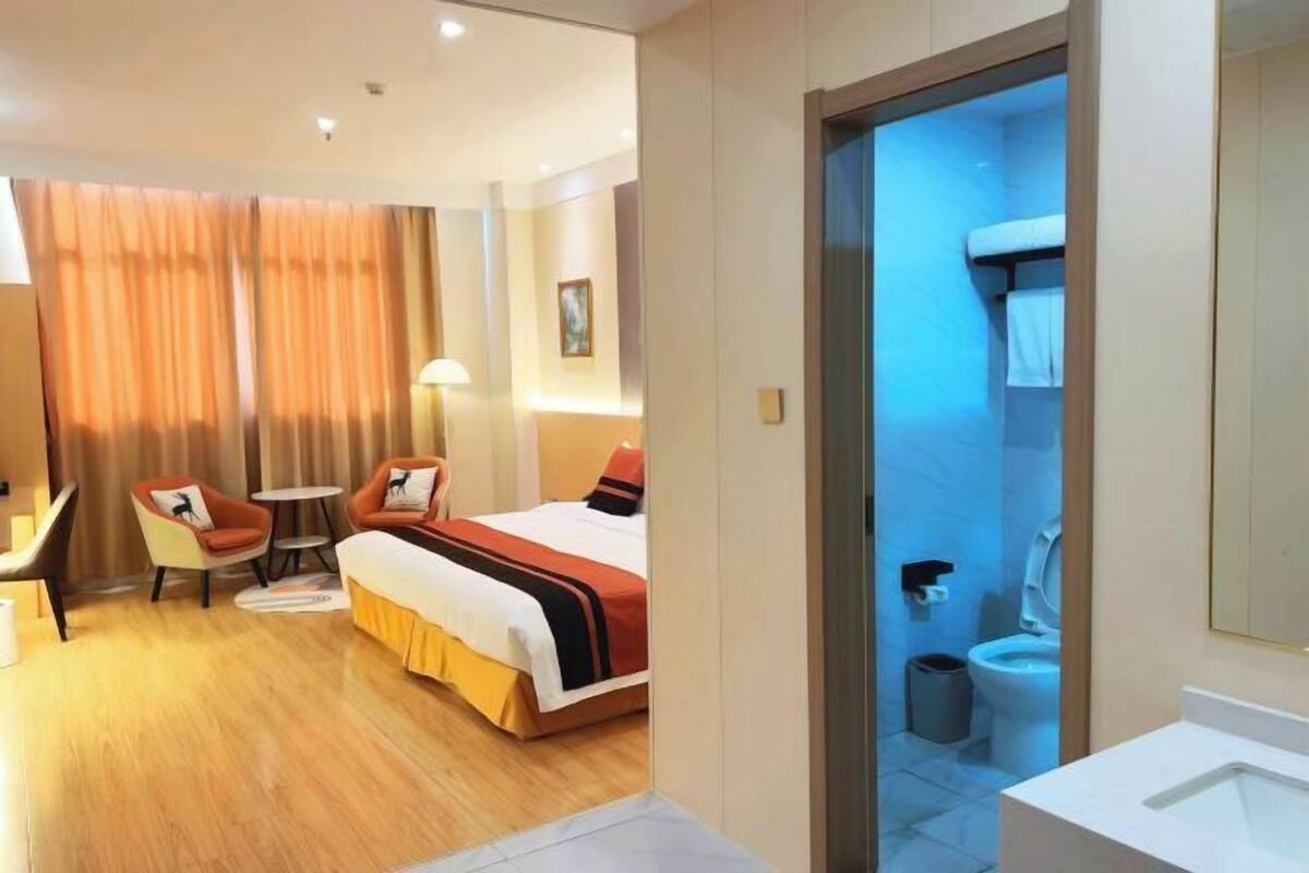 Une chambre d’hôtel avec un lit, un bureau, une chaise, une petite table et une salle de bain visible à travers une porte ouverte.