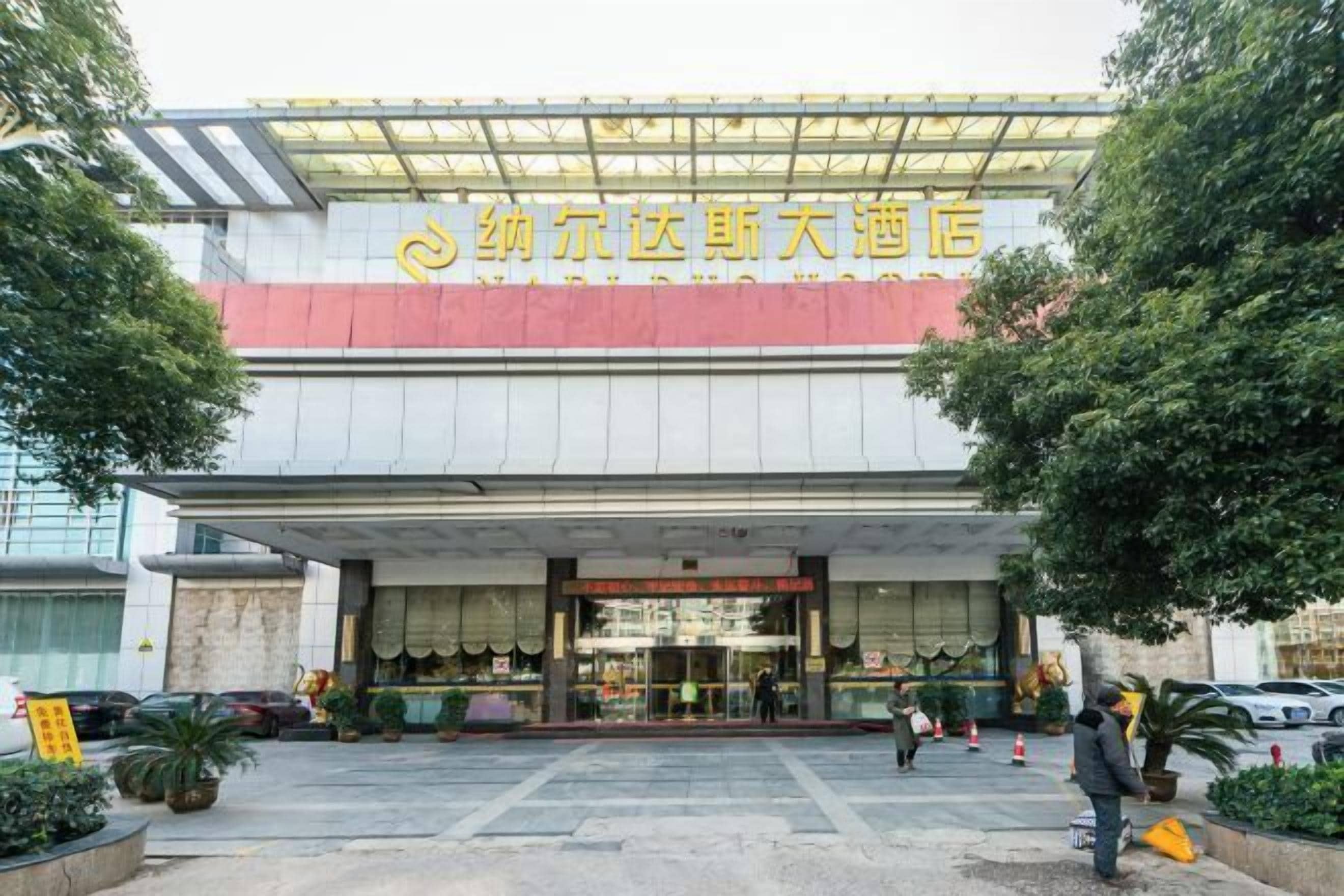 A hotel entrance with a large sign, a covered entrance, and a person standing near the entrance.