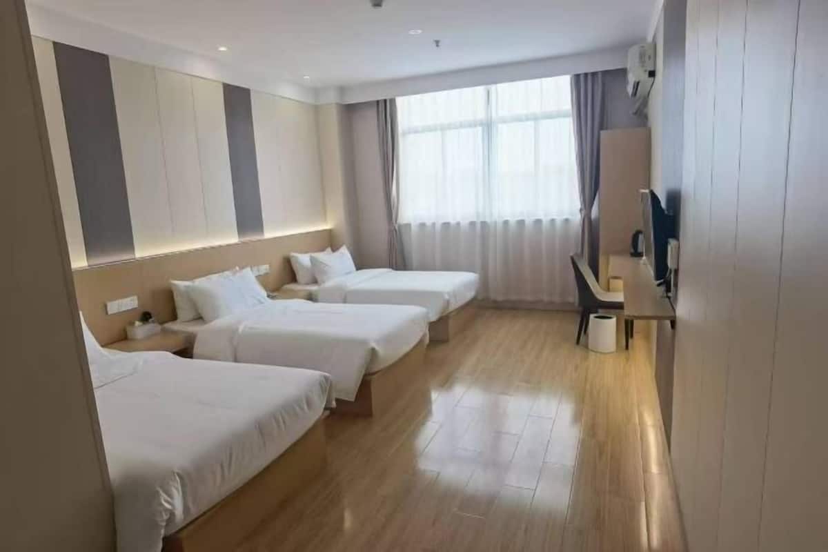 Une chambre d’hôtel avec trois lits, une télévision, un bureau et une fenêtre avec des rideaux.