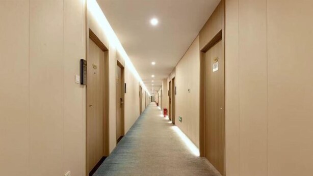 Un long couloir étroit, typique des hôtels, avec des portes des deux côtés, un sol recouvert de moquette et un éclairage encastré.