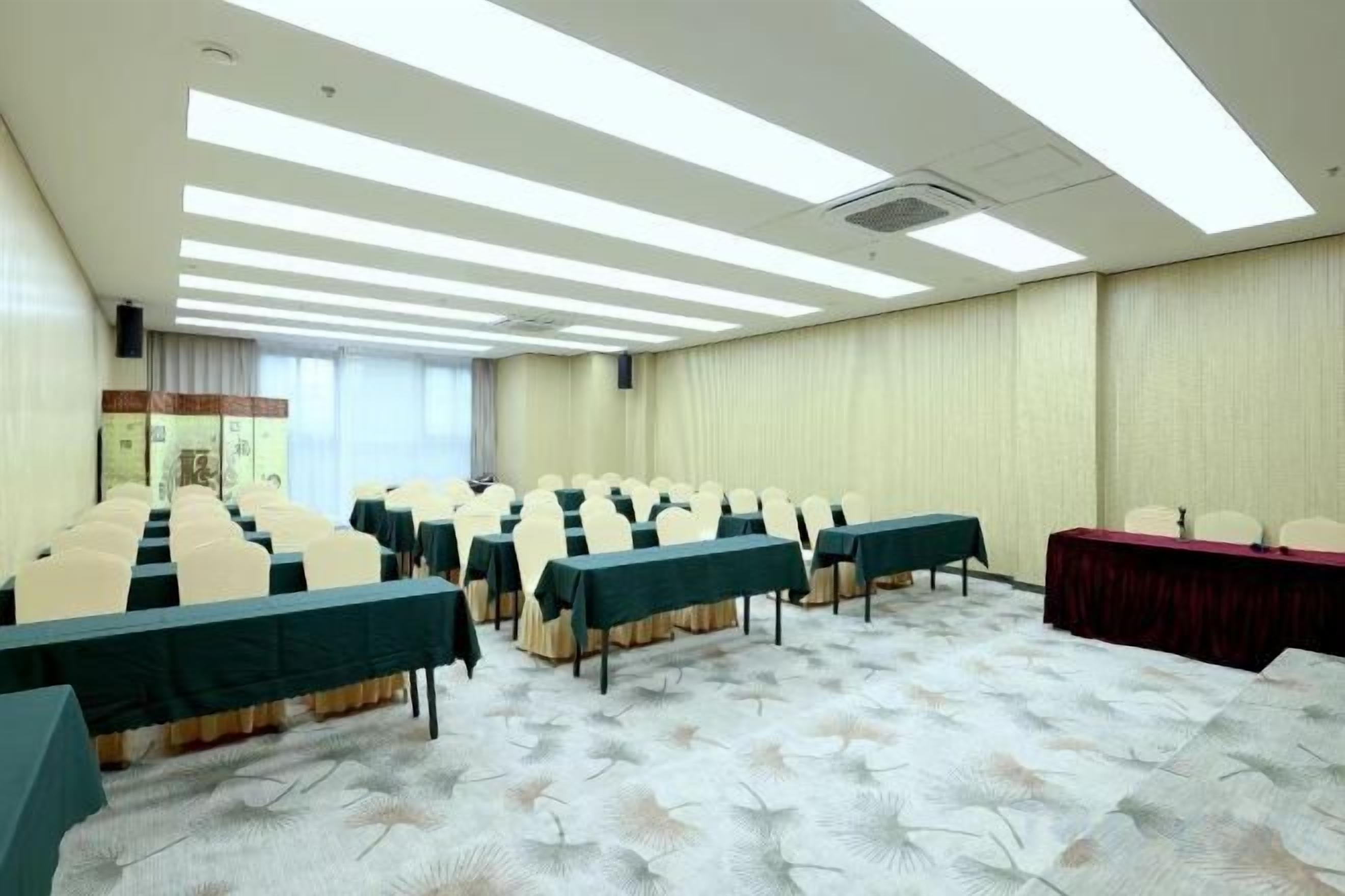 A conference room with rows of tables and chairs, a stage, and a carpeted floor.