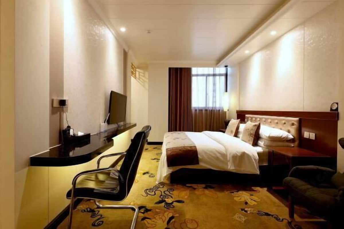 Une chambre d’hôtel avec un lit, un bureau, une chaise, une télévision et une fenêtre avec des rideaux.