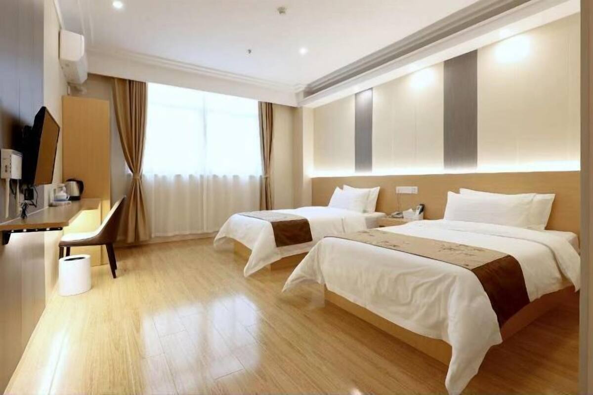 Une chambre d’hôtel avec deux lits, un bureau, une chaise et une grande fenêtre avec des rideaux.