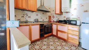 A kitchen with wooden cabinets, a stainless steel range hood, a microwave, a refrigerator, and patterned floor tiles.