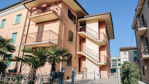 A multi-story residential building with balconies, a gated entrance, and a clear sky.