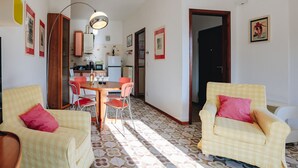 A dining area with a table and chairs, a kitchen in the background, and a patterned floor.