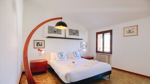 A bedroom with a bed, a nightstand, a red lamp, a radiator, and framed pictures on the wall.