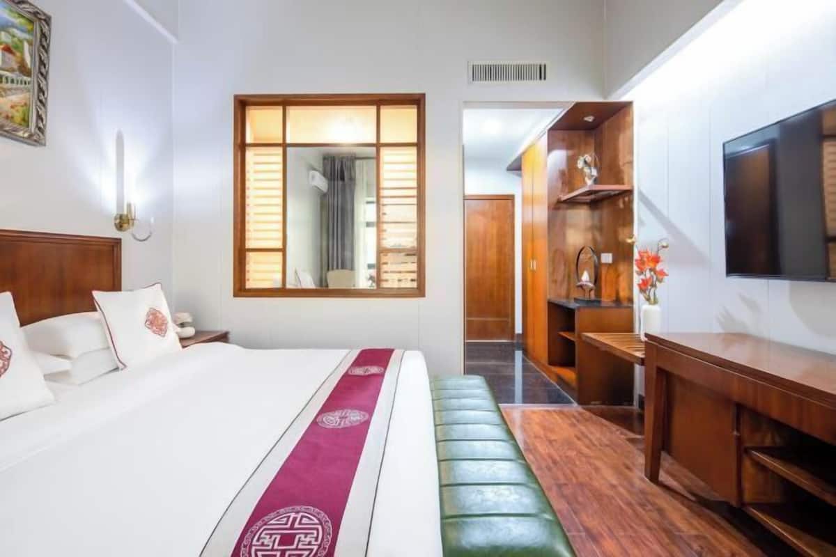 Habitación de hotel con cama, banca, televisor, mueble de madera y espejo.