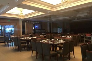 Un restaurante con varias mesas y sillas, un candelabro y una zona con escenario.
