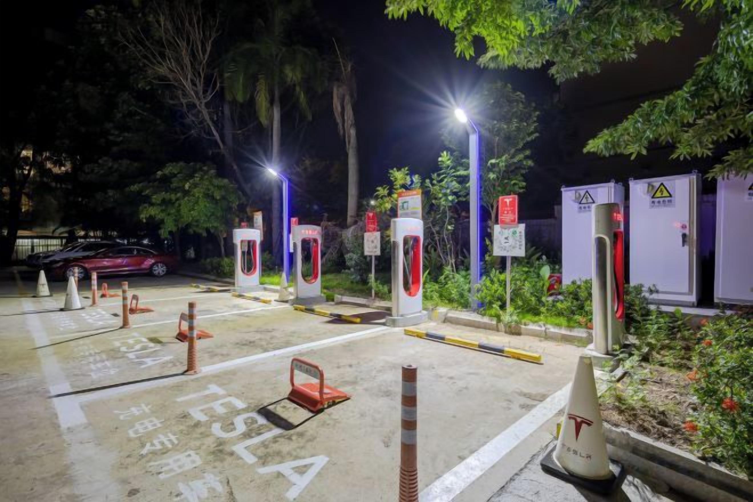 A parking area with marked spaces for electric vehicles, charging stations, and safety cones.