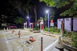 Un área de estacionamiento con espacios delimitados para vehículos eléctricos, estaciones de carga y conos de seguridad.