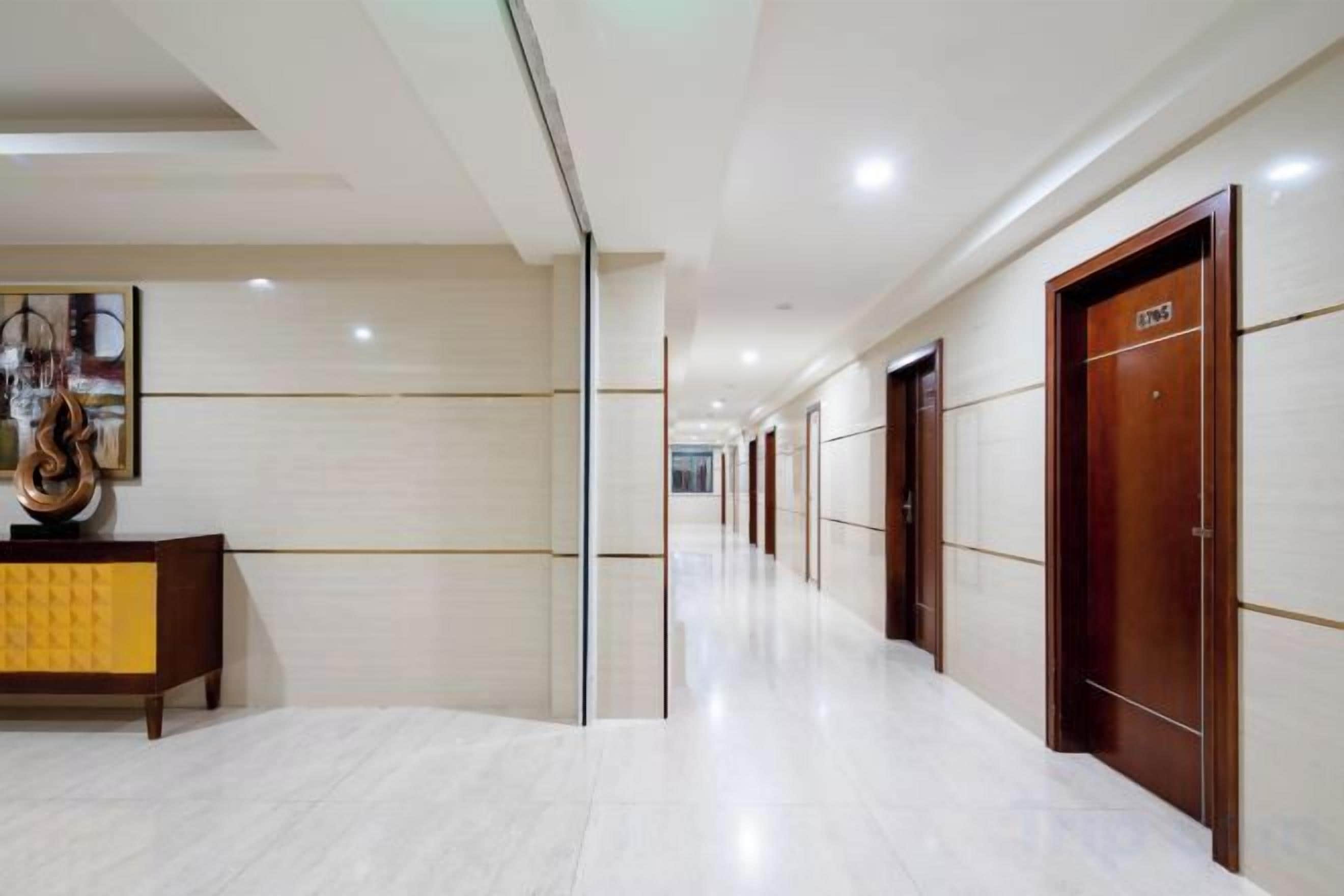 A hotel corridor with a marble floor, wooden doors, and a reception area with a decorative piece.