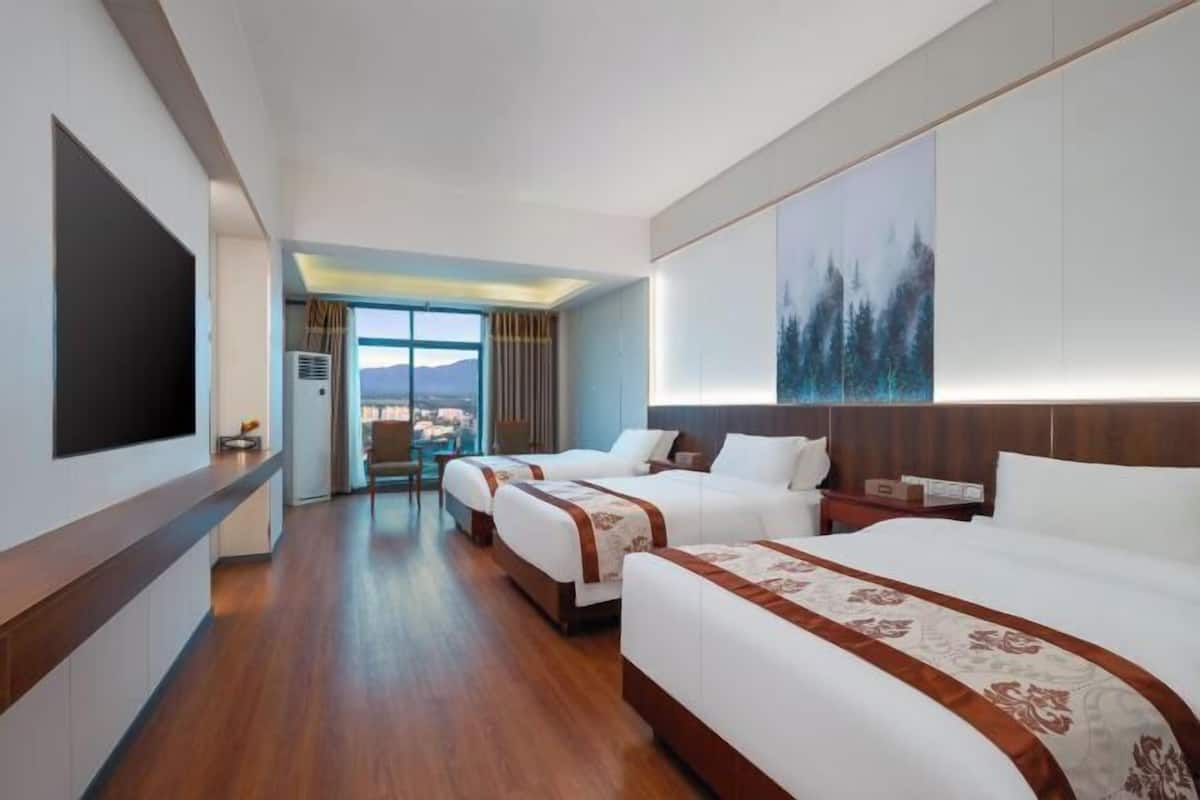 Habitación de hotel con dos camas, un ventanal grande y vistas a la montaña.