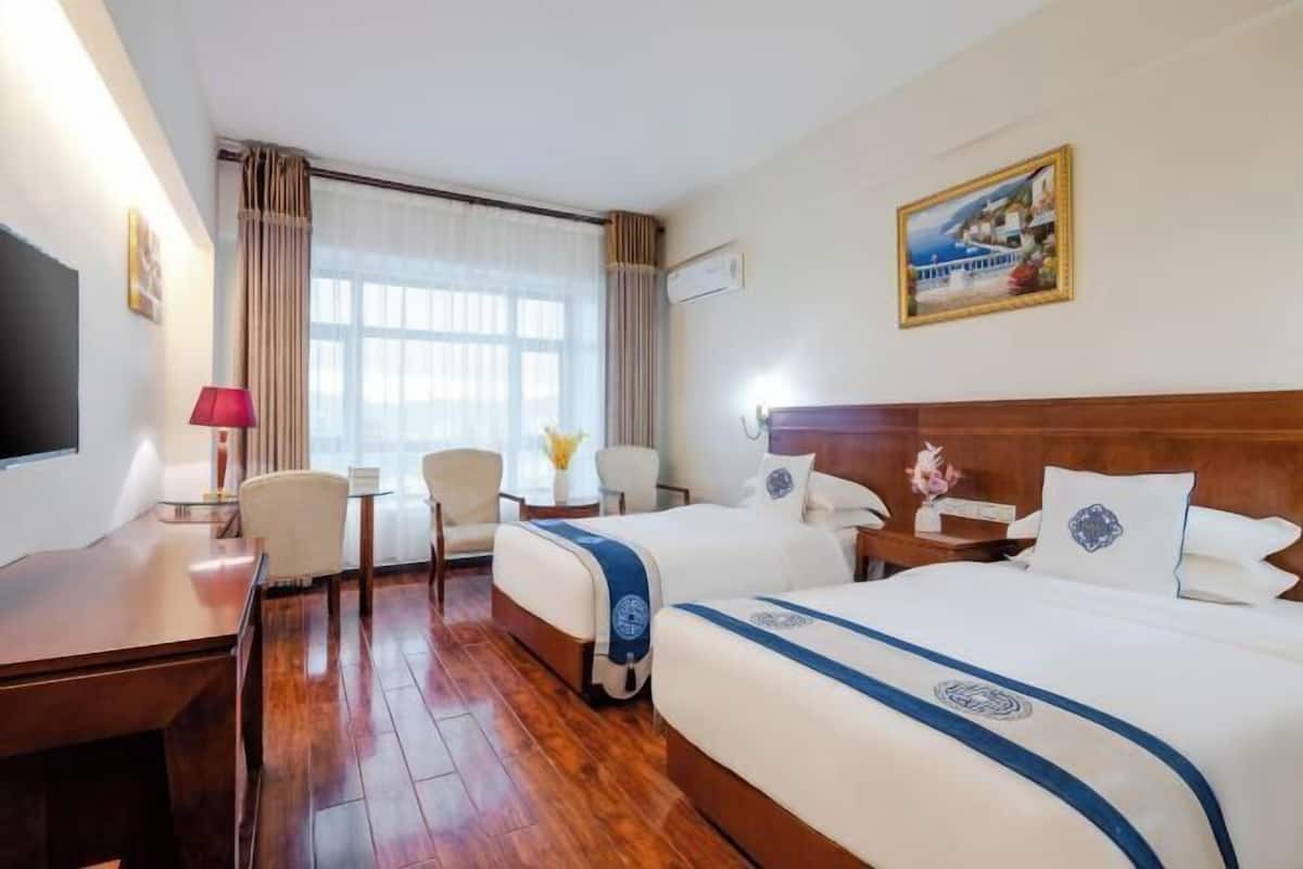 Una habitación de hotel con dos camas, un escritorio, una silla, un televisor y un cuadro en la pared.