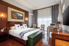 Een hotelkamer met een groot bed, een groene gestoffeerde bank, een bureau met een stoel, een televisie en een schilderij aan de muur.