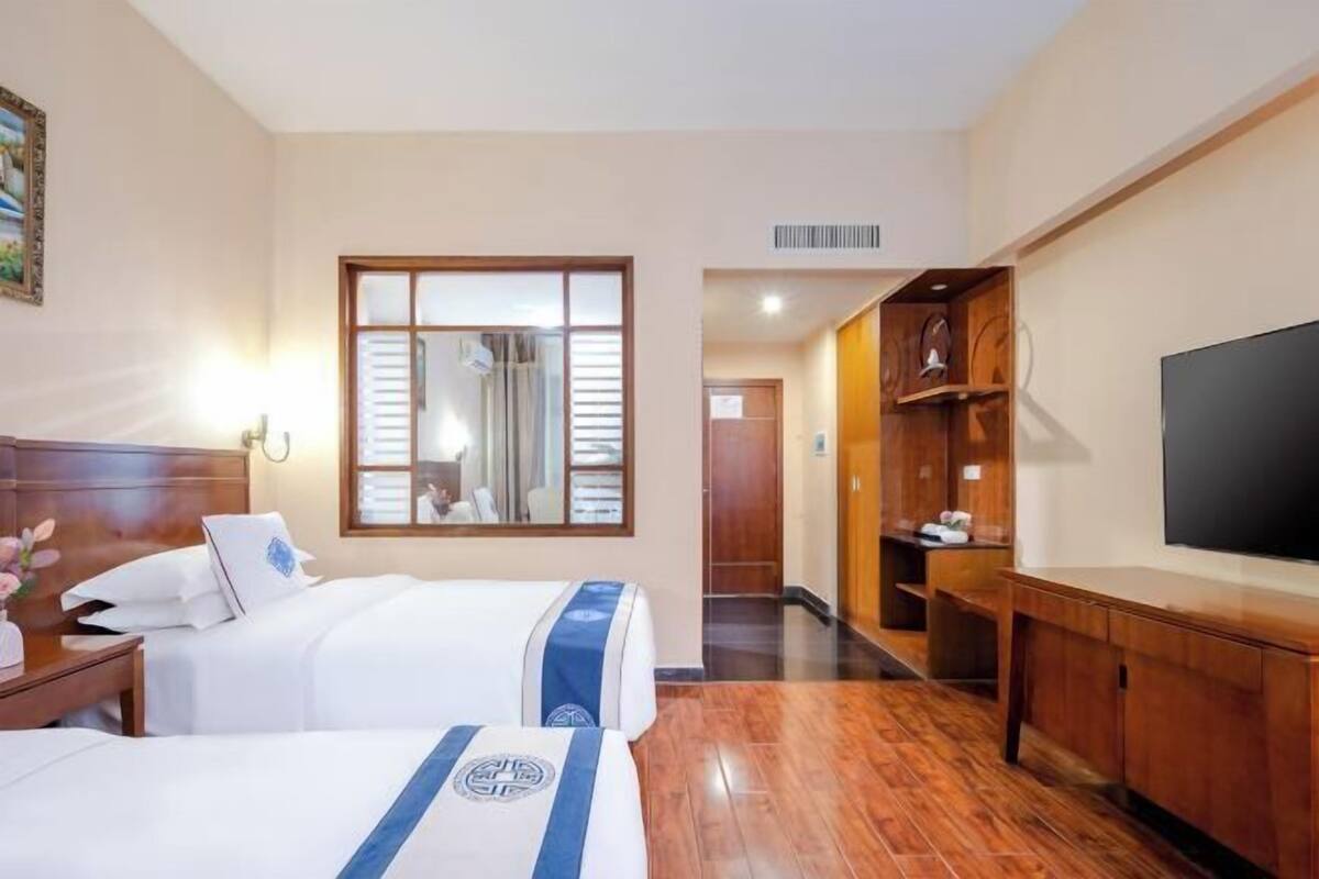 Habitación de hotel con dos camas, televisión, suelo de madera y un ventanal grande.