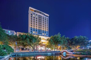 Un hôtel au design moderne, agrémenté d’un bassin d’eau décoratif à l’avant et doté d’une façade bien éclairée.