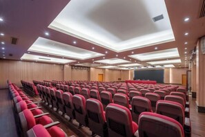 Une salle de conférence avec des rangées de chaises, une scène et un écran de projection.