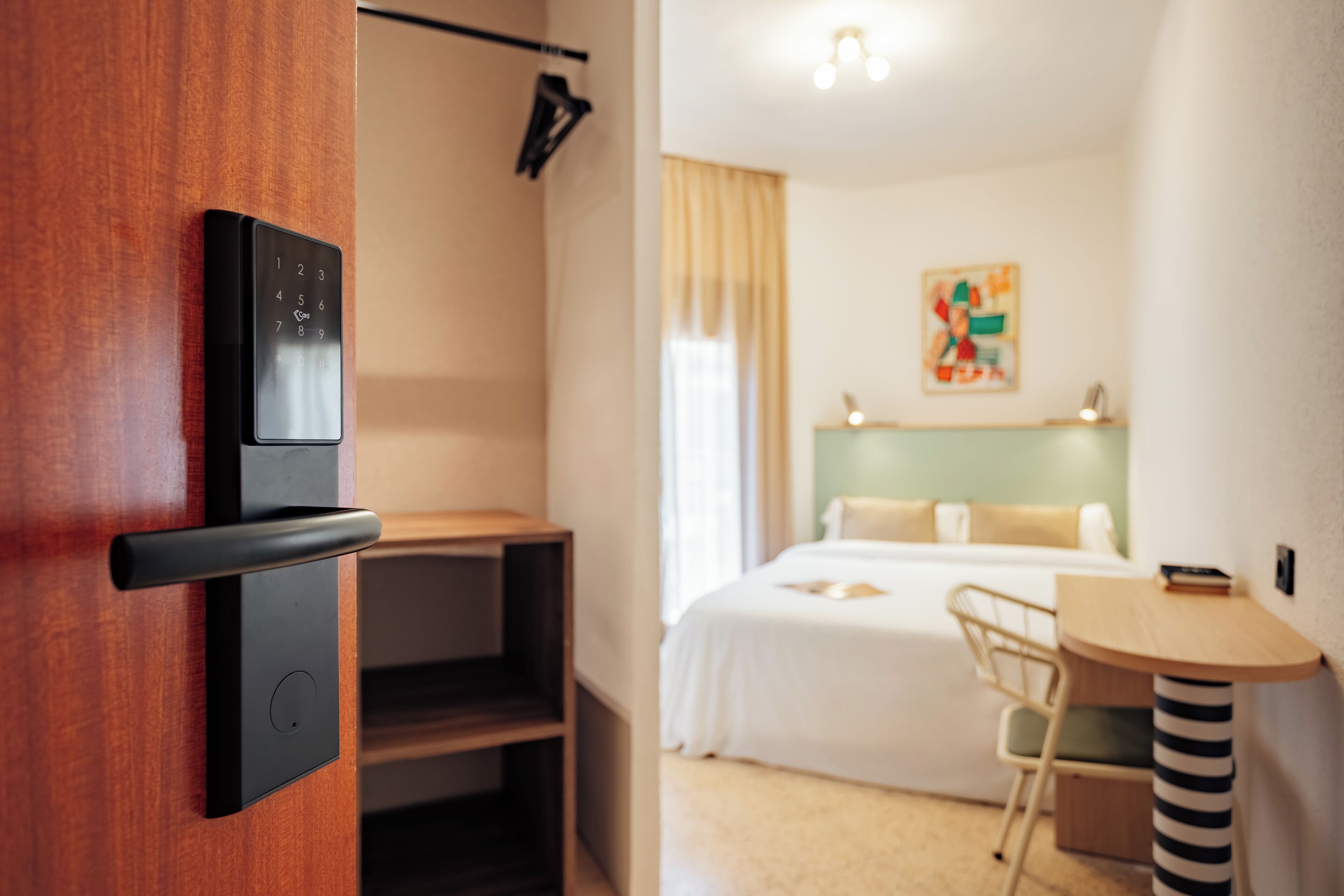 Une chambre d’hôtel moderne avec une porte en bois, un lit doté d’une tête de lit verte, un bureau et une chaise.