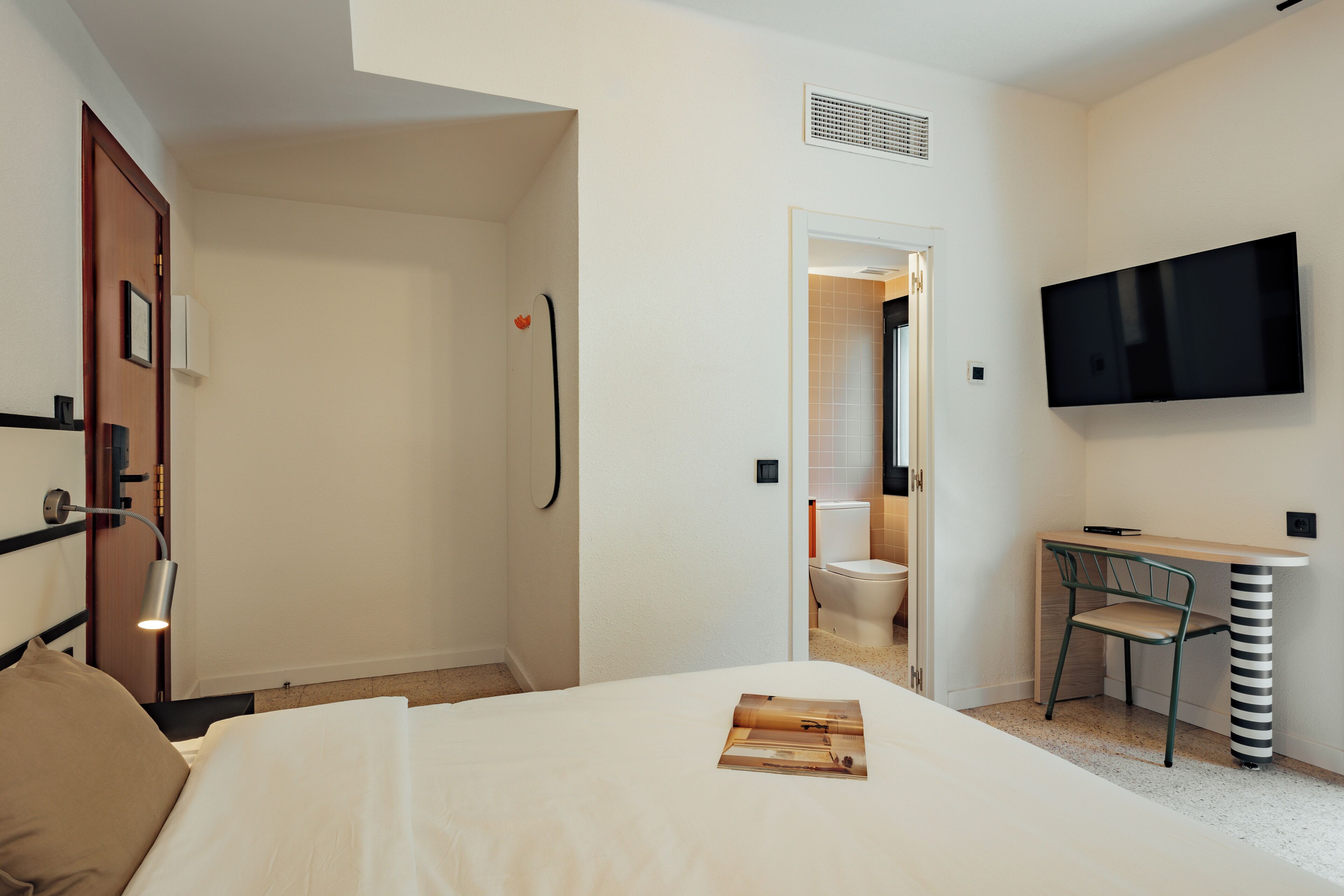 A hotel room with a bed, a desk with a chair, a television, and a bathroom visible through an open door.