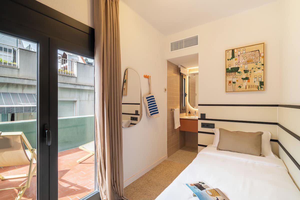 A hotel room with a bed, a bathroom, and a view of the outside balcony.