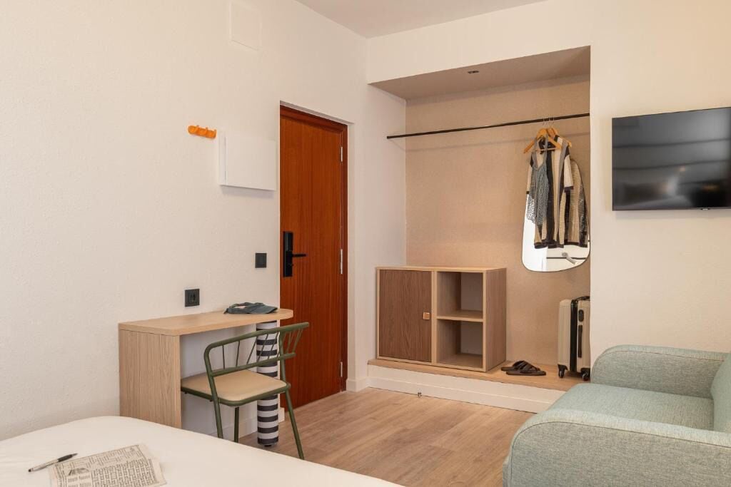 A compact room with a bed, a desk with a chair, a wardrobe, and a TV mounted on the wall.