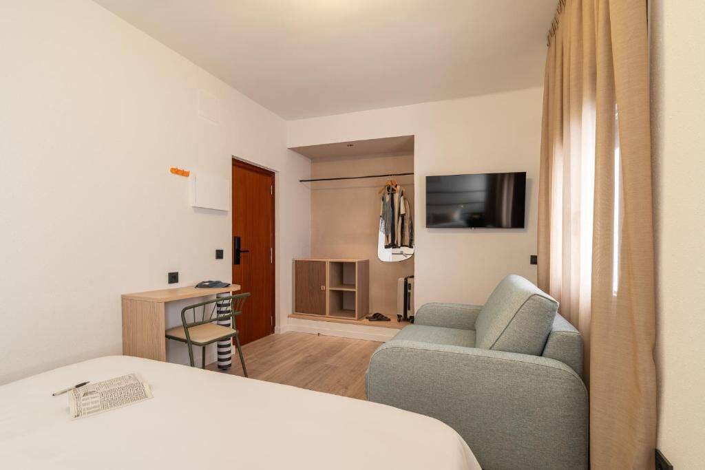 A hotel room with a bed, a desk, a chair, a wardrobe, a television, and a sofa.