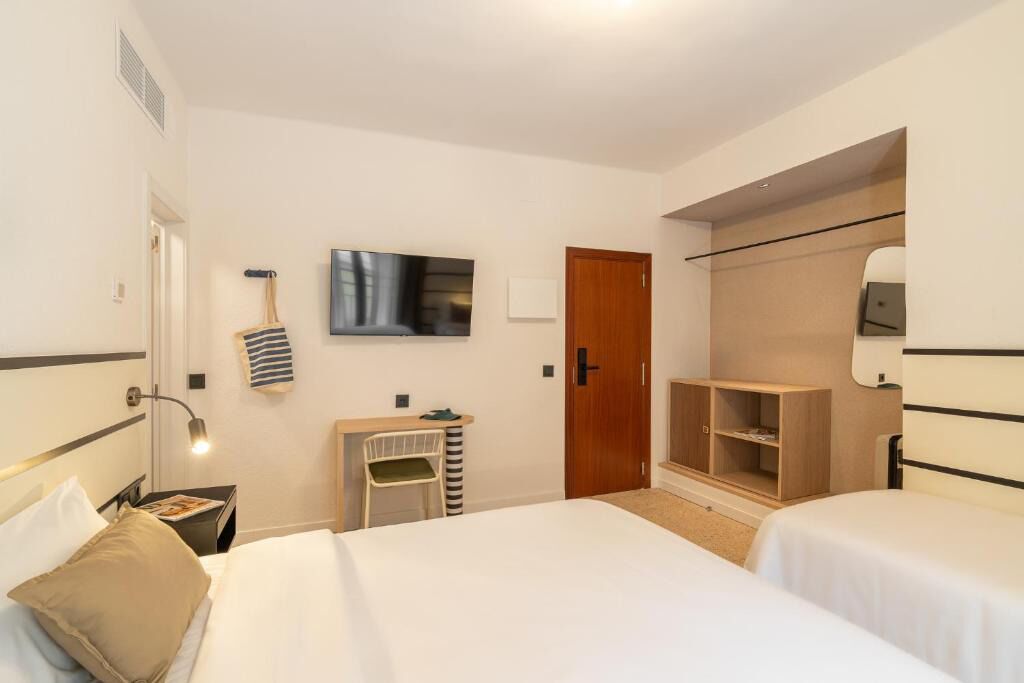 Une chambre d’hôtel avec deux lits, une télévision, une armoire, un bureau et une chaise.