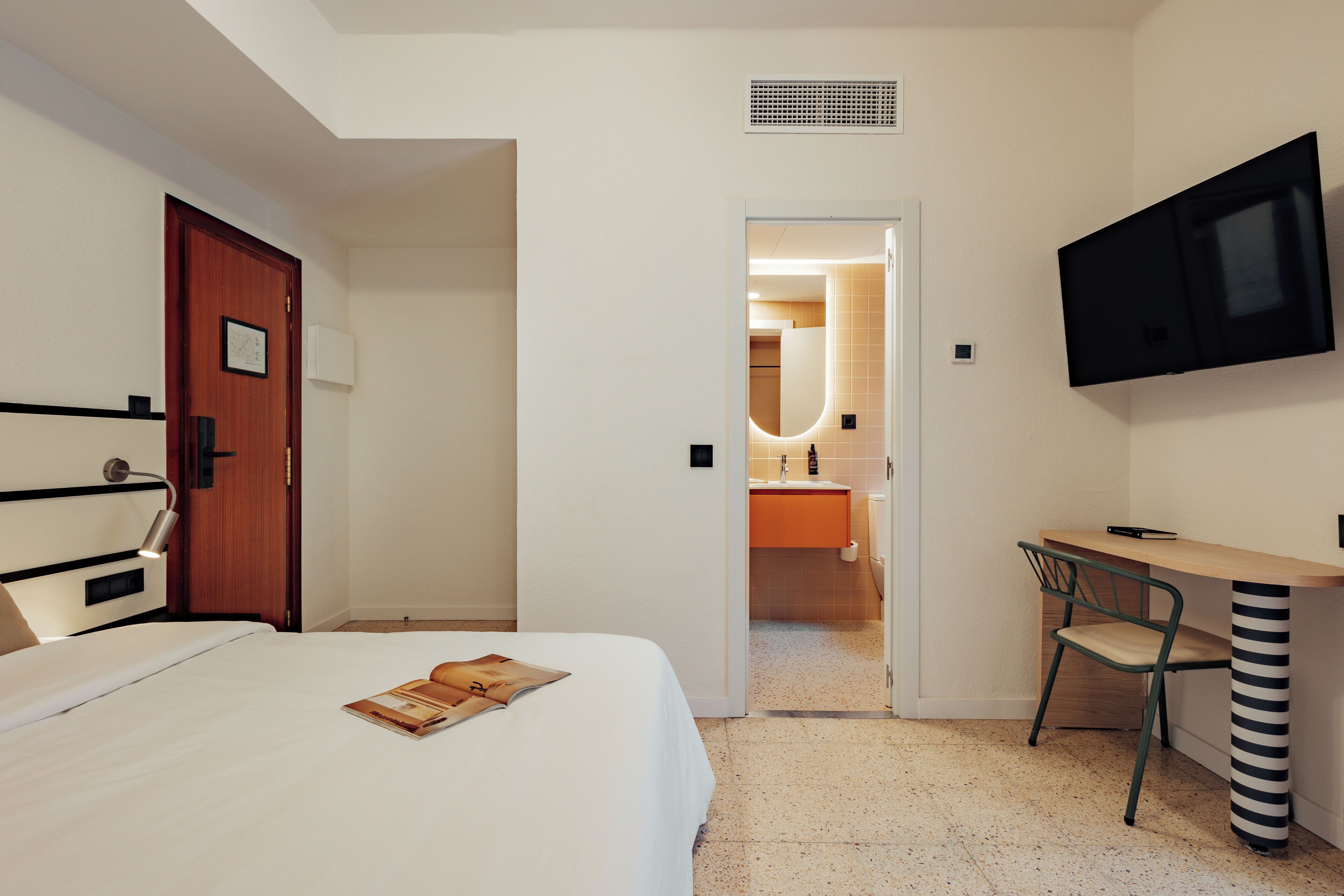 Ein Hotelzimmer mit einem Bett, einem Schreibtisch, einem Sessel, einem Fernseher und einem durch eine offene Tür einsehbaren Badezimmer.
