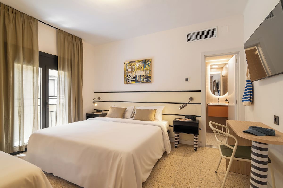 A hotel room with a large bed, a desk with a chair, a mirror, and a painting on the wall.